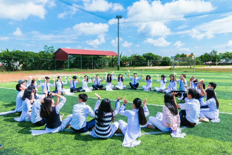 A group of people sat on a grass field on an unknown day.